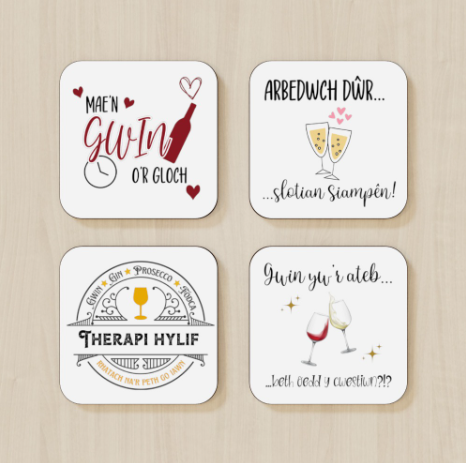 A set of four square coasters with rounded edges, each featuring a different Welsh language phrase about coffee and tea, with corresponding English translations and imagery like cups and hearts.