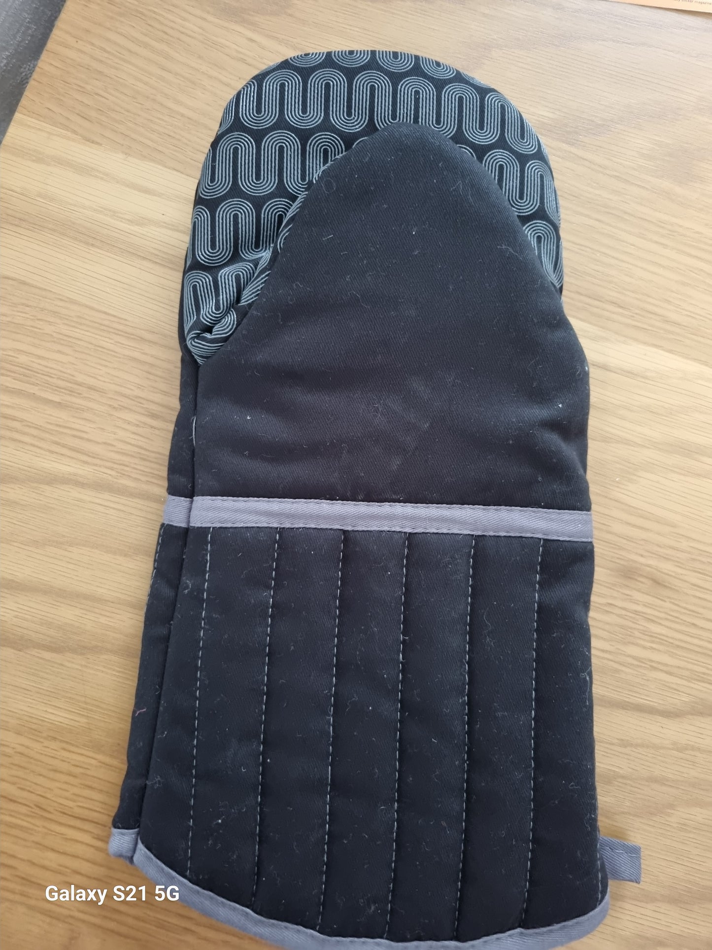 Black oven mitt with gray interior on a wooden surface