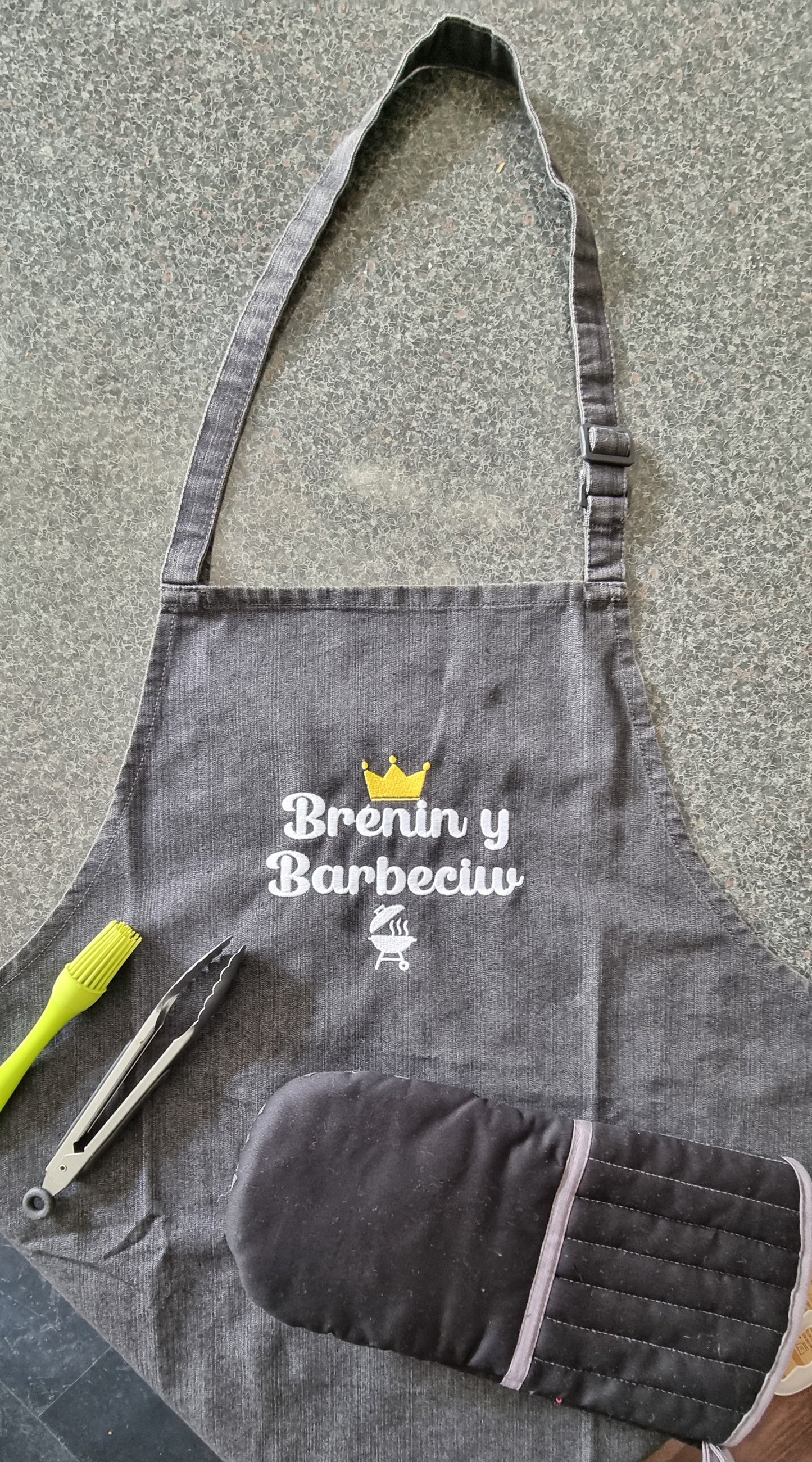 Gray apron with BBQ tools on a stone surface