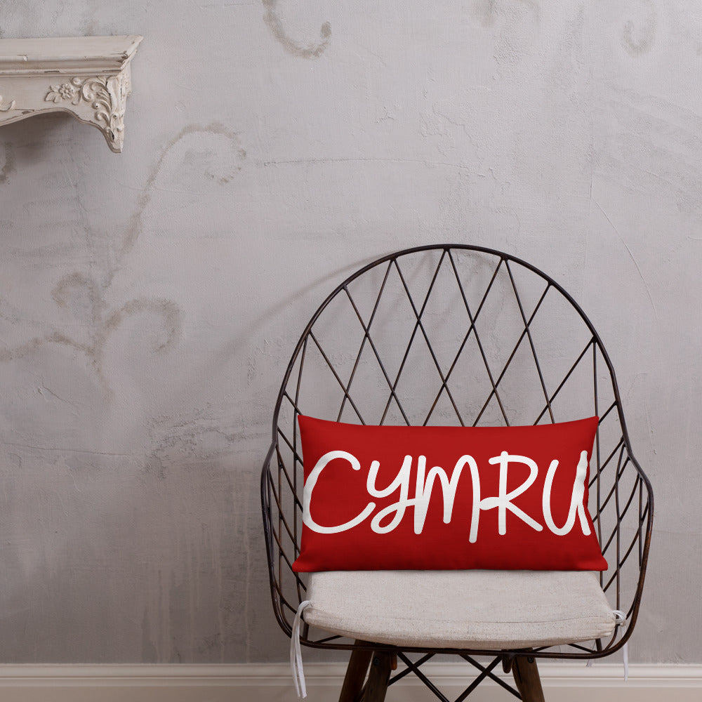 A premium pillow with a Welsh themed design, featuring text in Welsh on a sofa in a room with decorative plants and wooden furniture.