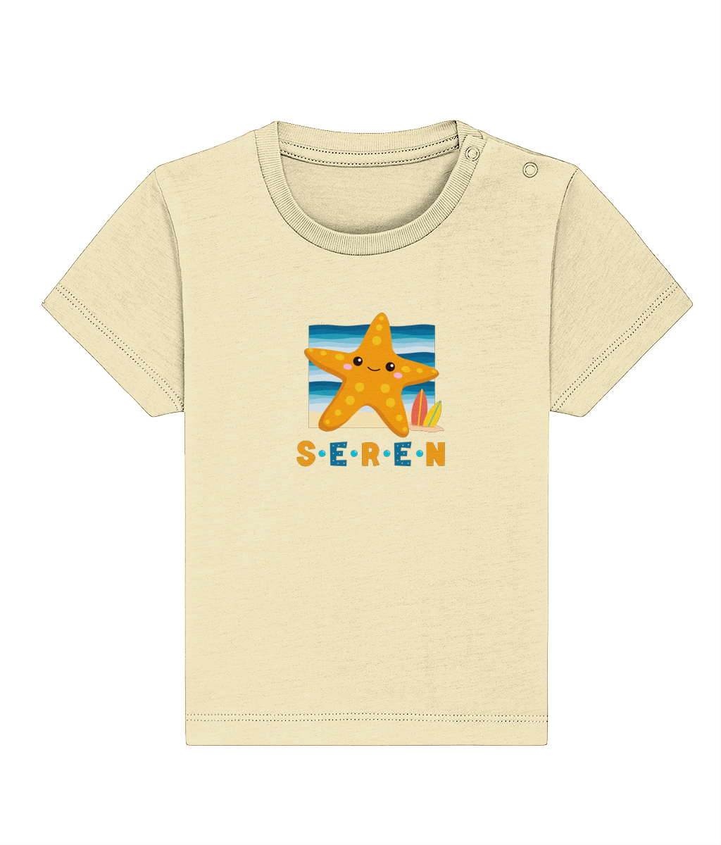 A baby t-shirt in a light color with the name 'Seren' printed on the front, featuring a graphic of a starfish and a sunset or sunrise scene.