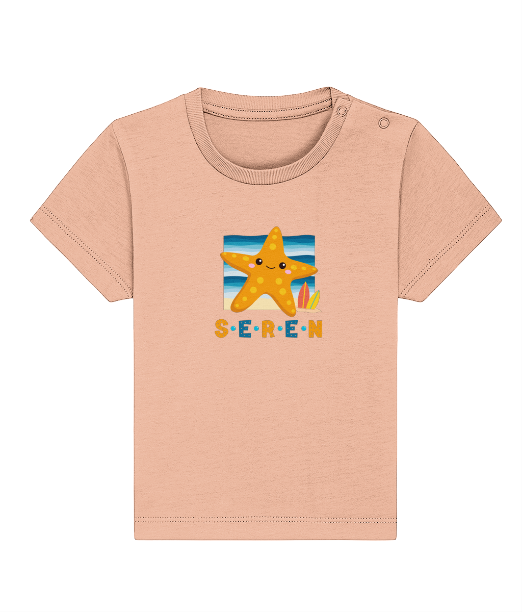 A baby t-shirt in a light color with the name 'Seren' printed on the front, featuring a graphic of a starfish and a sunset or sunrise scene.