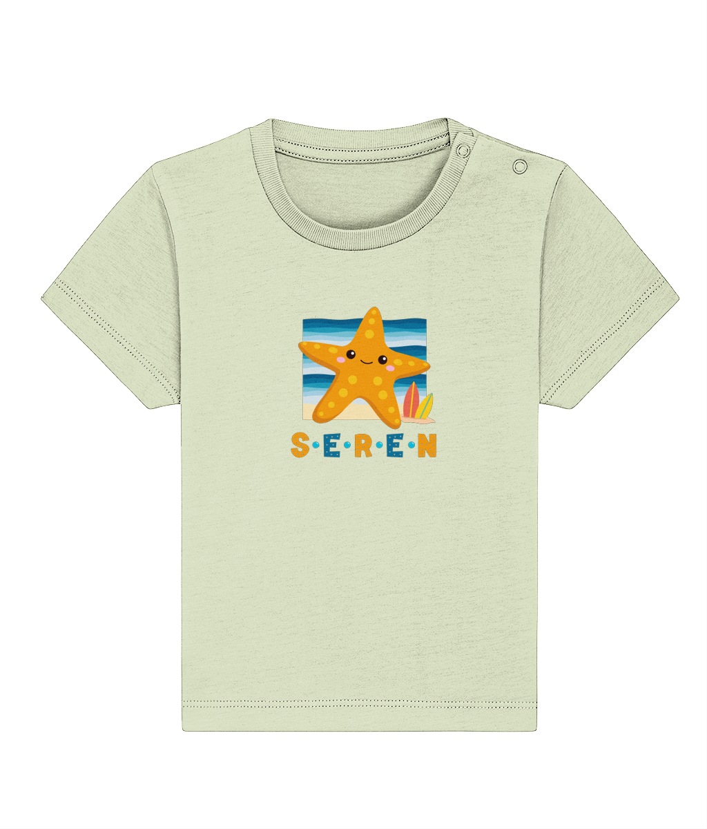 A baby t-shirt in a light color with the name 'Seren' printed on the front, featuring a graphic of a starfish and a sunset or sunrise scene.