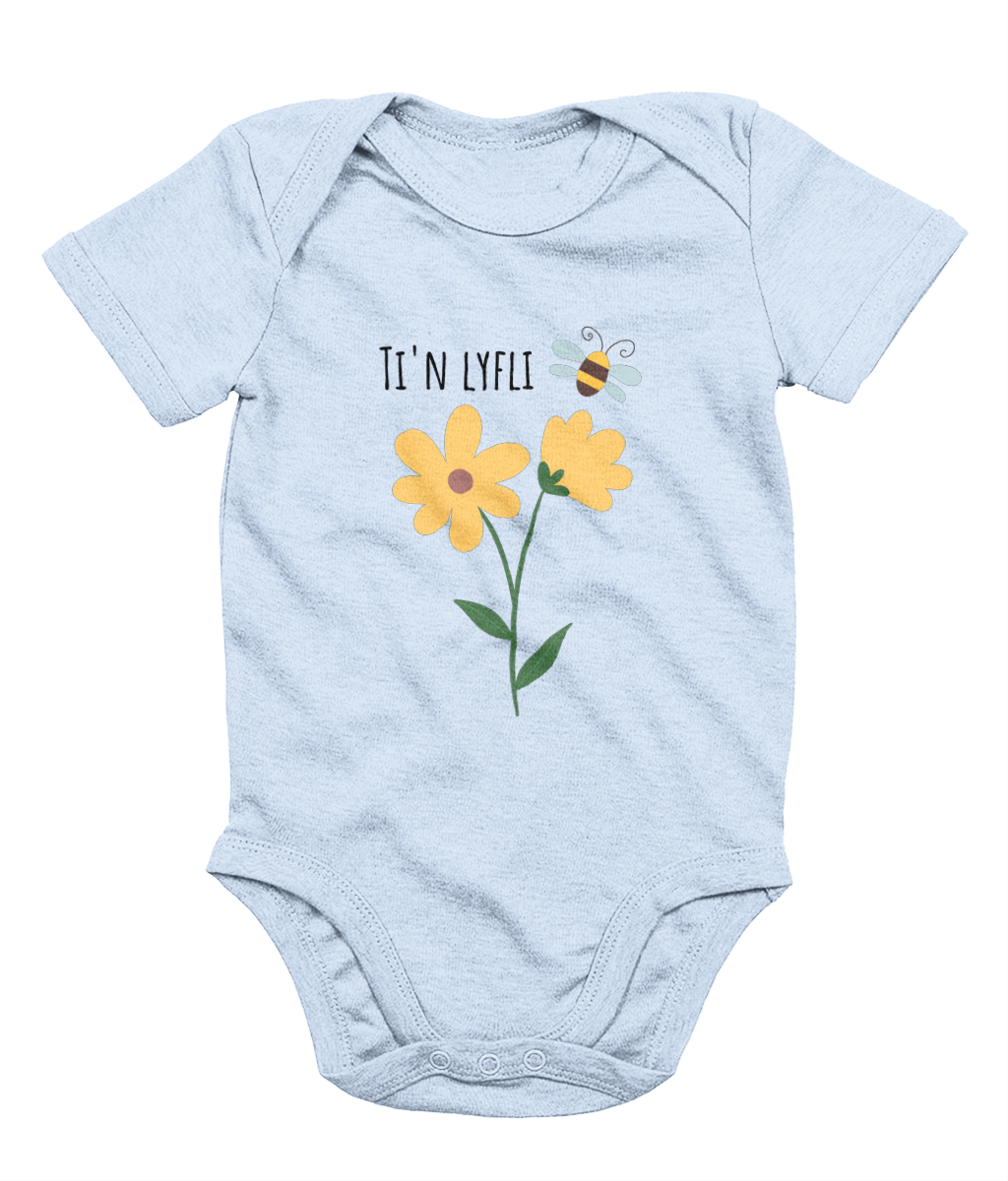 A blue babygrow with a graphic print of a sunflower and a bee, and the Welsh phrase 'Ti'n Lyfli' written in the center.