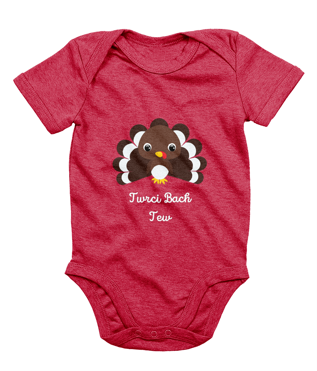 A red Welsh babygrow with a festive design featuring a character resembling a turkey and the text 'Twrci Bach Tew'.