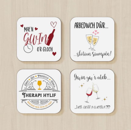 A set of four square coasters with rounded edges, each featuring a different Welsh language phrase about coffee and tea, with corresponding English translations and imagery like cups and hearts.