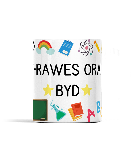 A white ceramic mug with a bold wraparound design featuring Welsh text and various colorful icons related to education.