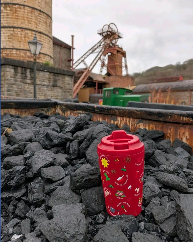 Red cup with colorful designs on a pile of coal in an industrial setting