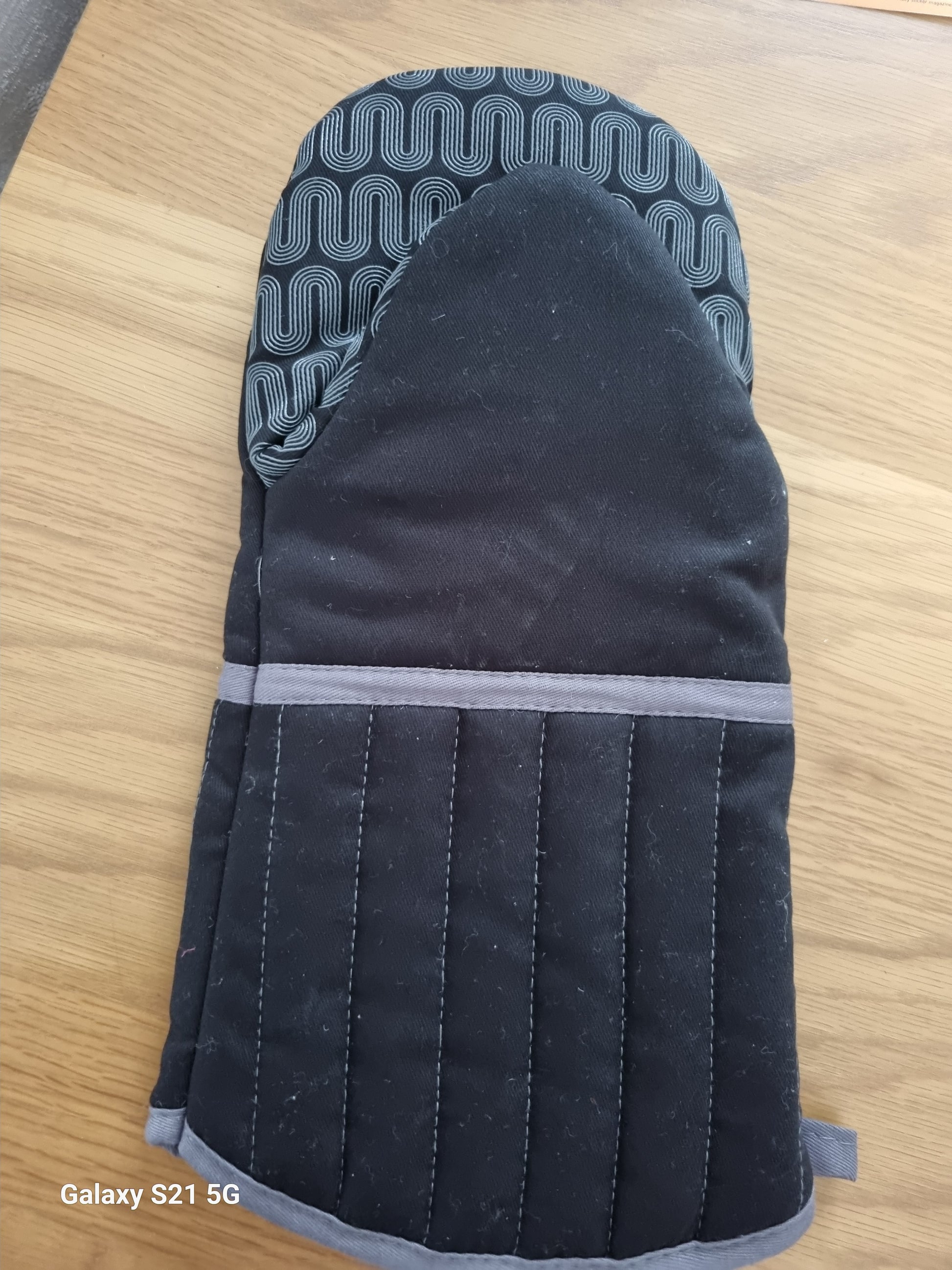 Black oven mitt with gray interior on a wooden surface