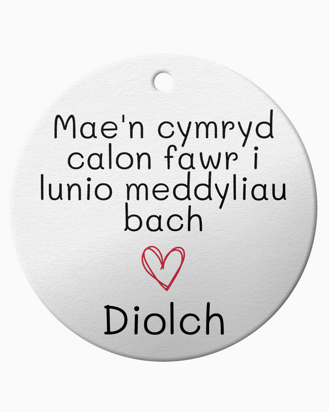 A white ceramic ornament with the Welsh phrase 'Mae'n cymryd calon fawr i lunio meddyliau fach' which translates to 'It takes a big heart to shape little minds', and the word 'Diolch' meaning 'thank you'.