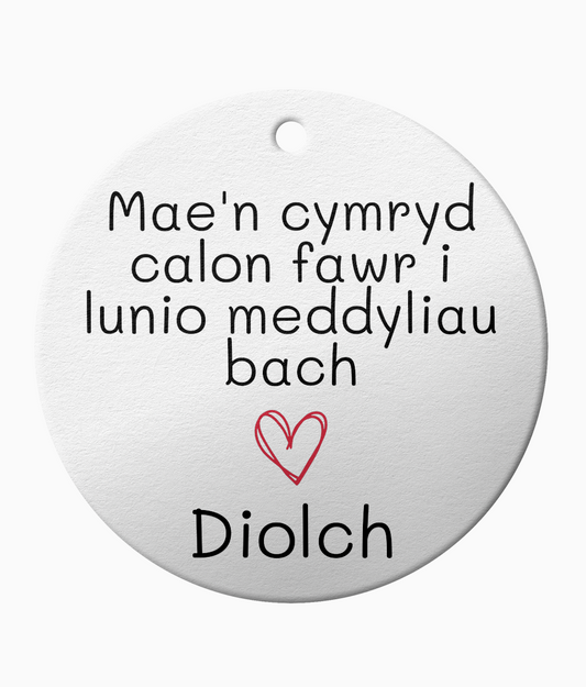 A white ceramic ornament with the Welsh phrase 'Mae'n cymryd calon fawr i lunio meddyliau fach' which translates to 'It takes a big heart to shape little minds', and the word 'Diolch' meaning 'thank you'.