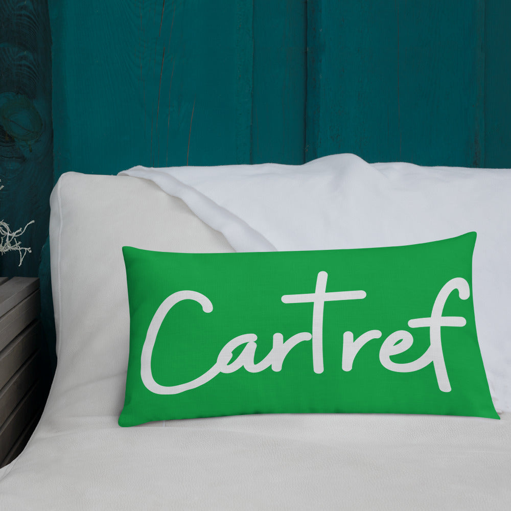 A premium pillow with a Welsh themed design, featuring text in Welsh on a sofa in a room with decorative plants and wooden furniture.