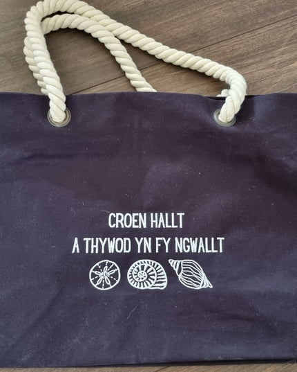 Navy blue tote bag with white text and rope handle on a wooden surface