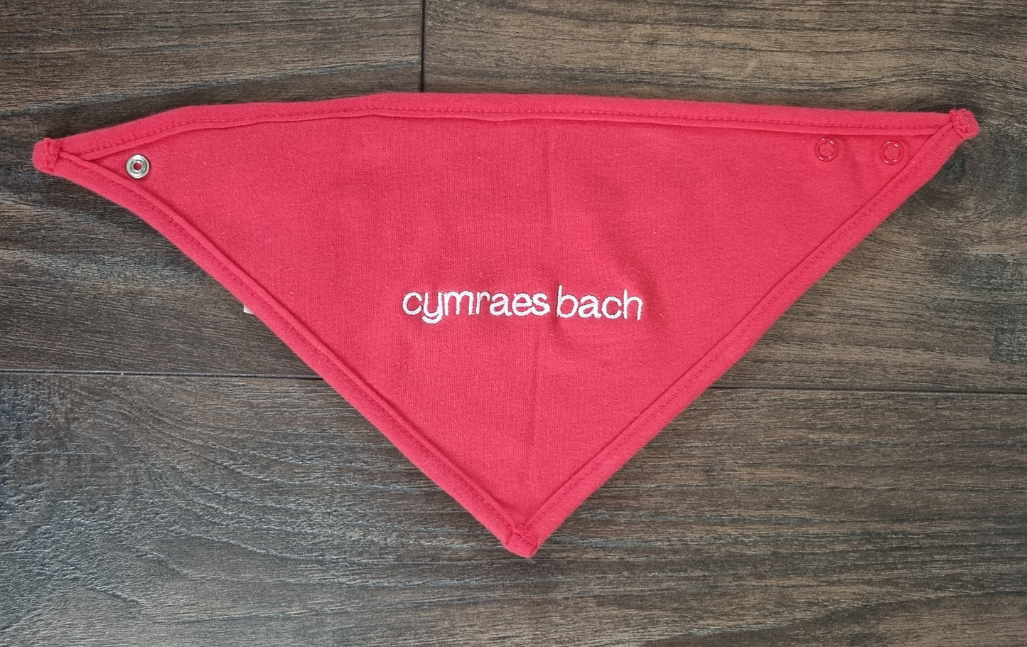 Red bandana cotton bib with 'cymraes bach' text on a wooden surface