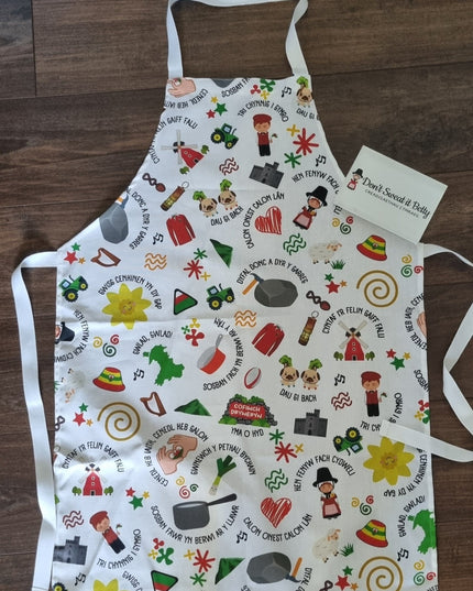 White cotton kitchen apron with welsh themed design on a wooden surface