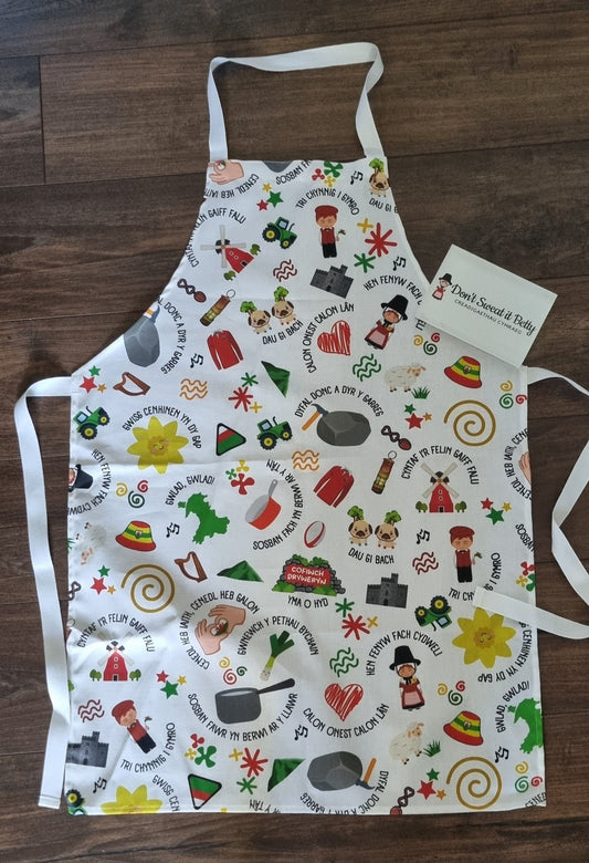 White cotton kitchen apron with welsh themed design on a wooden surface
