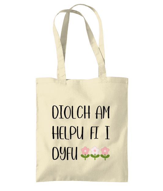 A beige cotton tote bag with the text 'Diolch am helpu fi i dyfu' printed in black.