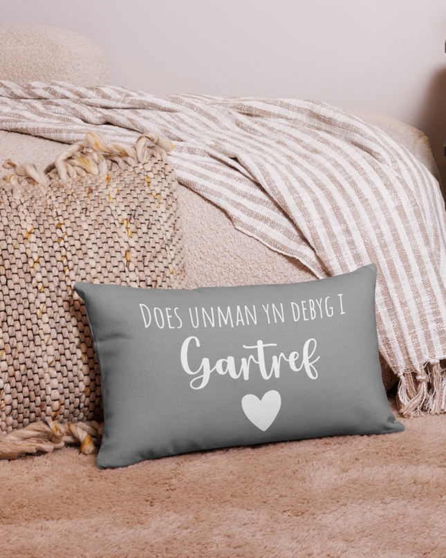 A premium pillow with a Welsh themed design, featuring text in Welsh on a sofa in a room with decorative plants and wooden furniture.