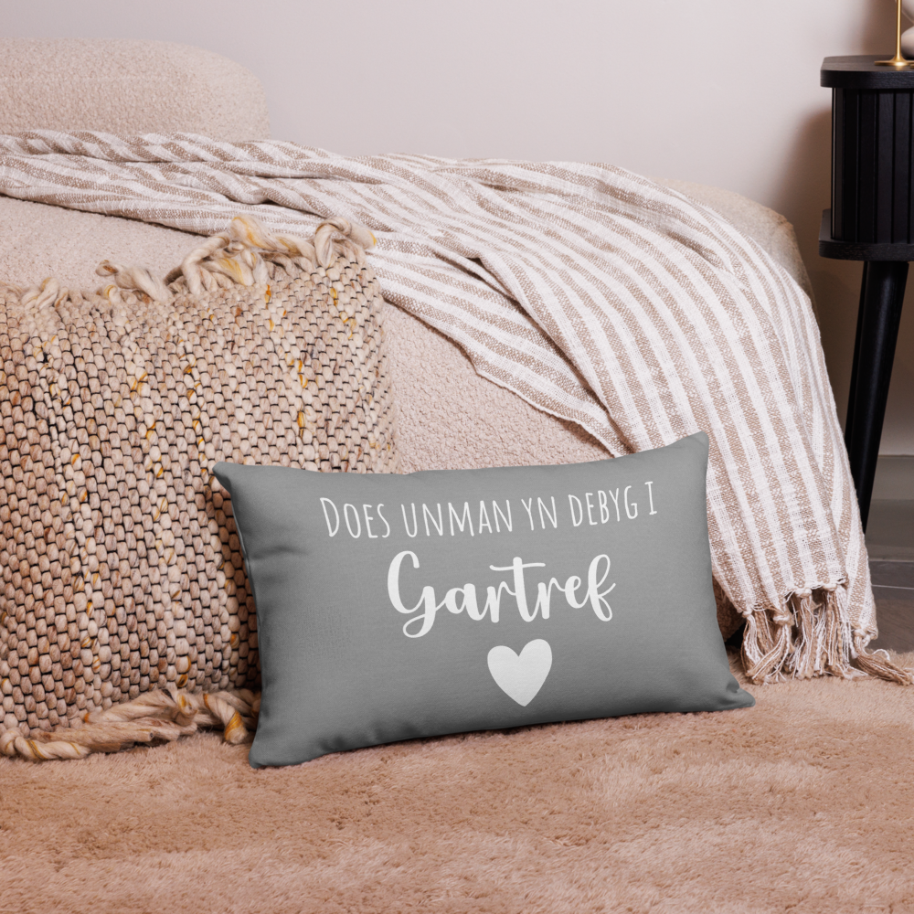 A premium pillow with a Welsh themed design, featuring text in Welsh on a sofa in a room with decorative plants and wooden furniture.