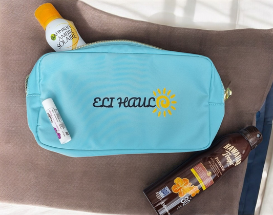 A blue waterproof suncream bag with the text 'Eli Haul' printed on the front, displayed on a neutral background alongside a suncream bottle and a spray bottle.
