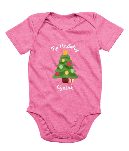 A pink babygro with 'Fy Nadolig Cyntaf' printed in Welsh, featuring a Christmas tree motif.