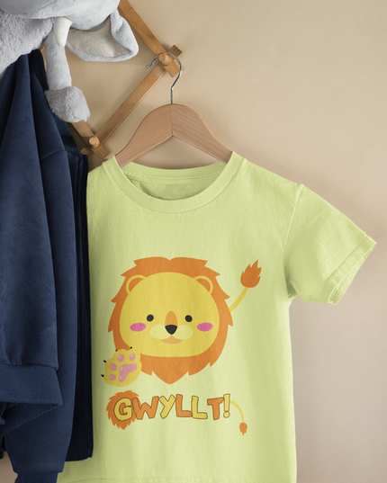 Child's T-shirt in pale yellow with a graphic of a lion's face and the word 'Gwyllt!' printed above it. The t-shirt is displayed on a wooden hanger next to a plush toy.