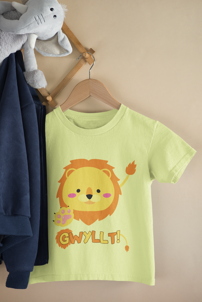 Child's T-shirt in pale yellow with a graphic of a lion's face and the word 'Gwyllt!' printed above it. The t-shirt is displayed on a wooden hanger next to a plush toy.