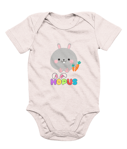 A pink babygrow with a graphic of a grey bunny and the text 'HOPUS' in bold, stylized lettering. The bunny has ears and carrots, suggesting a playful, Easter-themed design.