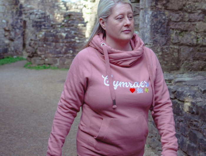 Person wearing a pink hoodie with 'Cymru' text in an outdoor setting.