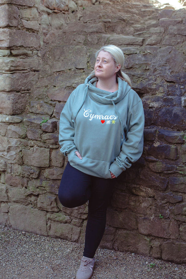 Person wearing a light blue hoodie leaning against a stone wall.