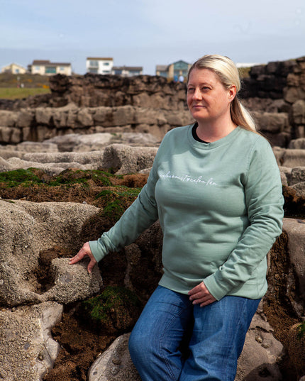Woman wearing a green sweatshirt with text, standing on stone steps with a scenic background.