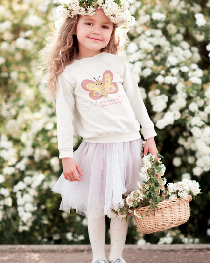 A young girl wearing a white sweatshirt with a butterfly graphic and the text 'ond cariad, be os wnei di hedfan?', holding a basket of flowers.