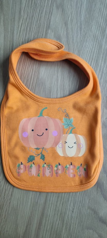 An orange baby bib with a pumpkin design and smaller pumpkins pattern.