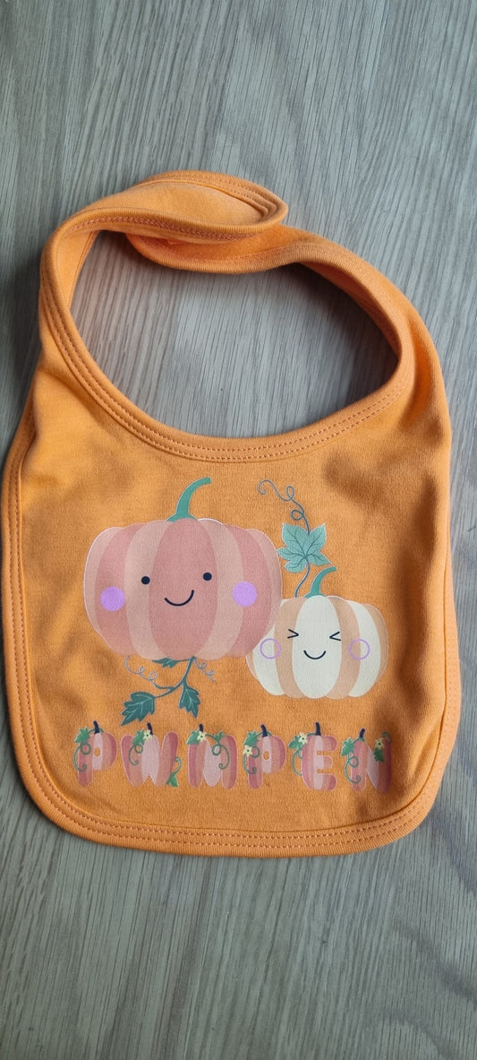 An orange baby bib with a pumpkin design and smaller pumpkins pattern.