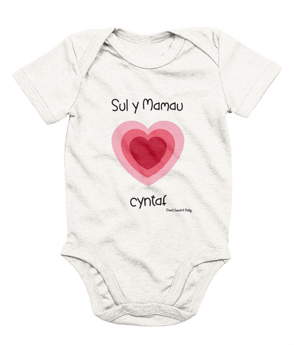 White baby bodysuit with a printed heart and the text 'Sul y Mamau cyntaf' in Welsh for 'First Mother's Day'.