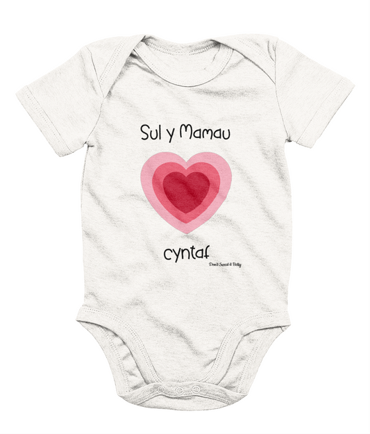 White baby bodysuit with a printed heart and the text 'Sul y Mamau cyntaf' in Welsh for 'First Mother's Day'.