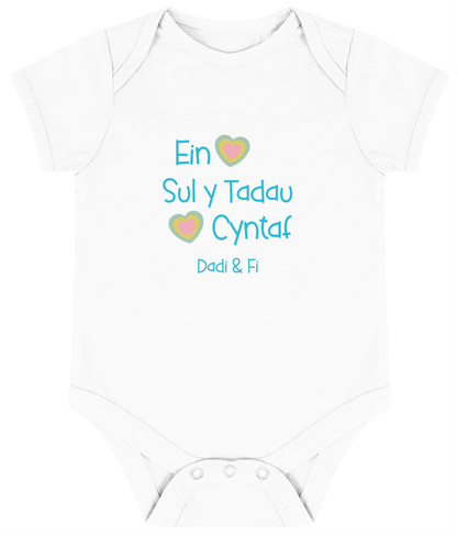 White babygrow with 'Ein Sul y Tadau Cyntaf' printed in blue, translates to 'Our First Father's Day' in Welsh.