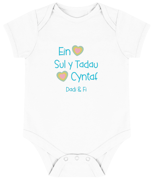 White babygrow with 'Ein Sul y Tadau Cyntaf' printed in blue, translates to 'Our First Father's Day' in Welsh.