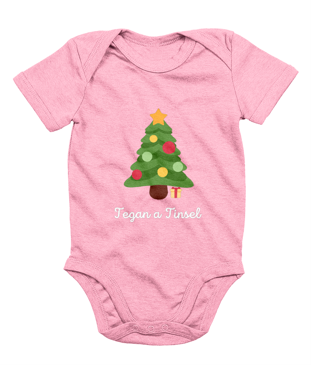 Pink Welsh Christmas-themed babygrow with a Christmas tree and gifts design, and the text 'Tegannau a Tinsel' printed on the front.