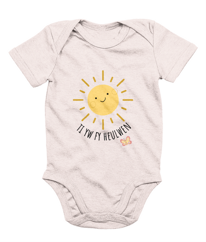 A baby pink babygrow with the text 'Ti yw fy heulwen' printed on the front, featuring a sun illustration and a small heart.