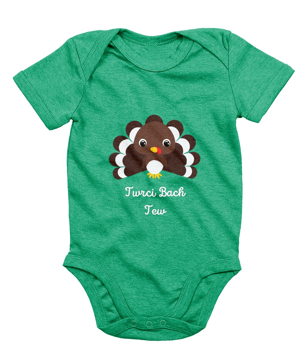 A green Welsh babygrow with a festive design featuring a character resembling a turkey and the text 'Twrci Bach Tew'.