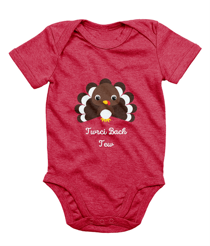 A red Welsh babygrow with a festive design featuring a character resembling a turkey and the text 'Twrci Bach Tew'.