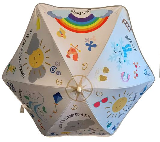 Children's umbrella with a Welsh-themed design featuring illustrations of the sun, clouds, rainbows, and Welsh phrases.