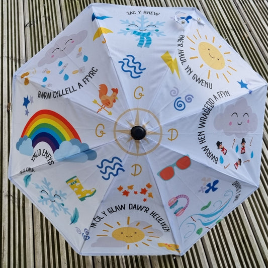 A Welsh themed umbrella with a printed design featuring weather-related motifs and Welsh text.