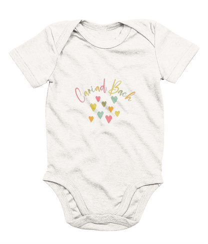 A white babygrow with 'Cariad Bach' text and colorful heart design in the center.