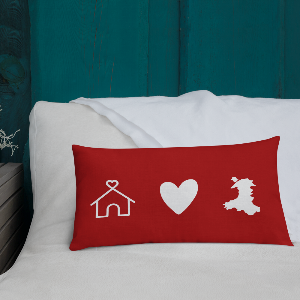 A premium pillow with a Welsh themed design, featuring text in Welsh on a sofa in a room with decorative plants and wooden furniture.