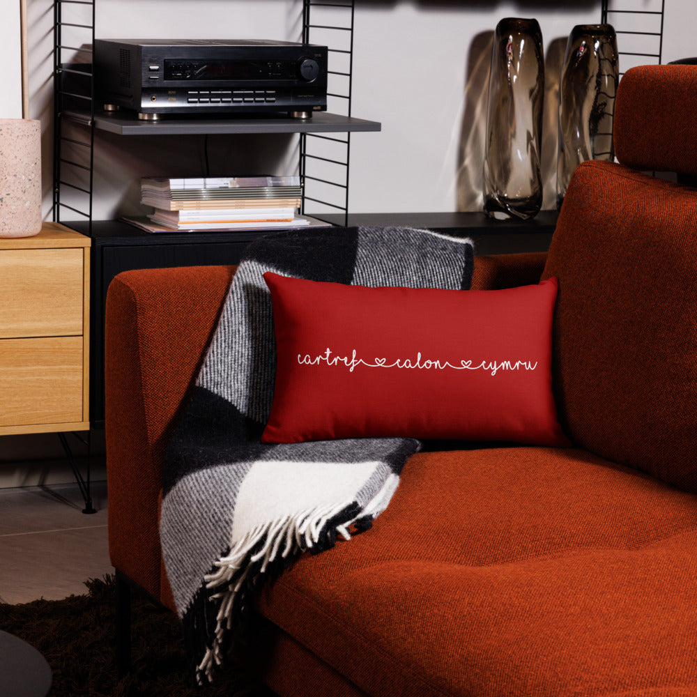 A premium pillow with a Welsh themed design, featuring text in Welsh on a sofa in a room with decorative plants and wooden furniture.