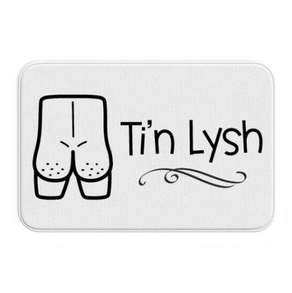 A white rectangular bath mat with a cartoon illustration of a peachy naked bottom and the text 'Ti'n Lysh' in Welsh.