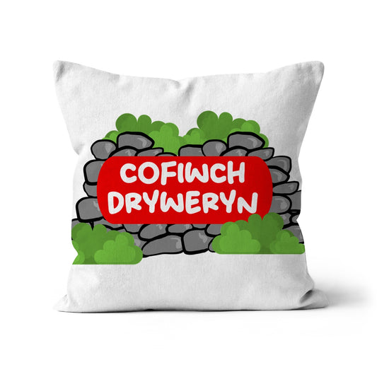 A cushion with a white background featuring the text 'COFIWCH DRYWERYN' in a red graffiti-style font, centered on a simulated grey concrete block pattern.