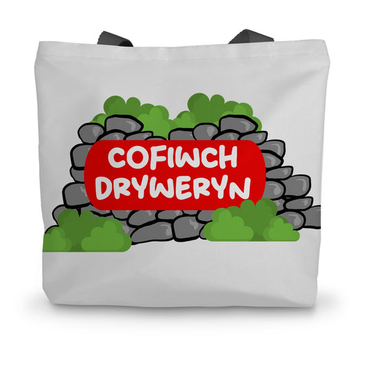 A white canvas tote bag with black handles featuring the text 'COFIWCH DRYWERYN' on a red background, designed to resemble a mural.